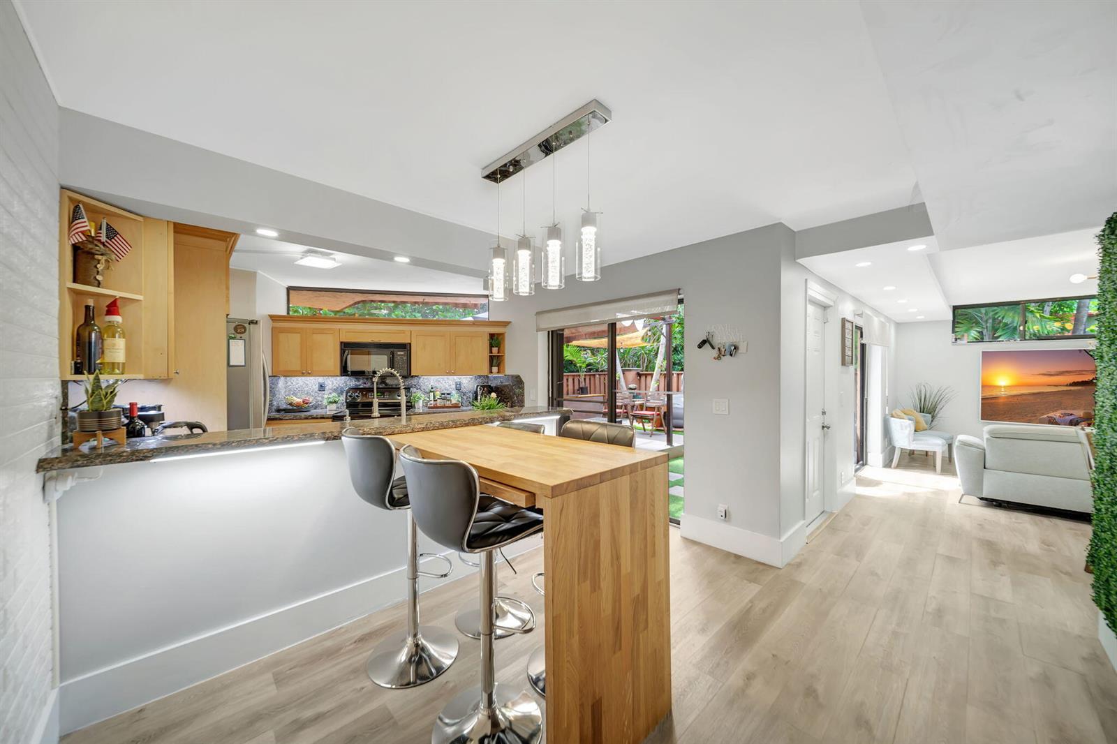 A kitchen with light wood cabinets and a breakfast bar opens to a living area — 8105 Severn Drive # C, Boca Raton FL 33433, BOCA RATON, FL