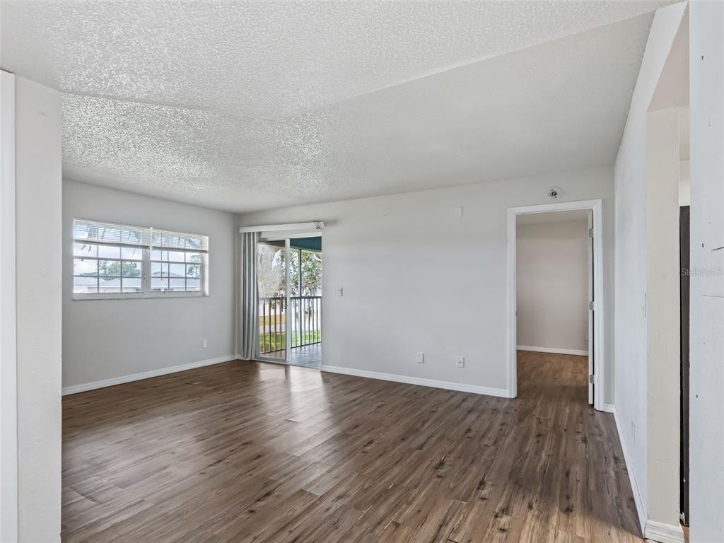 A living room with wood-look flooring, a sliding glass door to a balcony, and windows — 563 MIDWAY TRACK UNIT K203, OCALA, FL