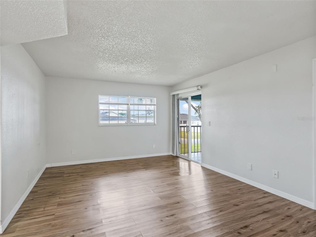 An empty room with wood-look flooring, a window, and a sliding glass door to a balcony — 563 MIDWAY TRACK UNIT K203, OCALA, FL