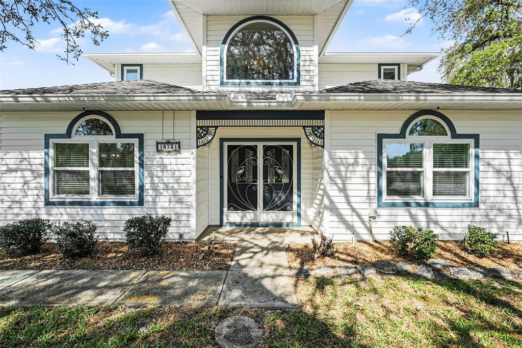 A white two-story house features a central arched window, double front doors, and dark trim — 18731 FIRETHORN DRIVE, SPRING HILL, FL