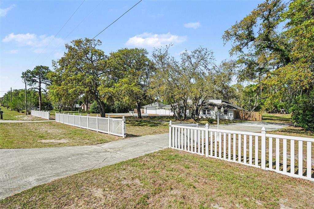 A white vinyl fence borders a concrete driveway leading toward a house and detached garage — 18731 FIRETHORN DRIVE, SPRING HILL, FL