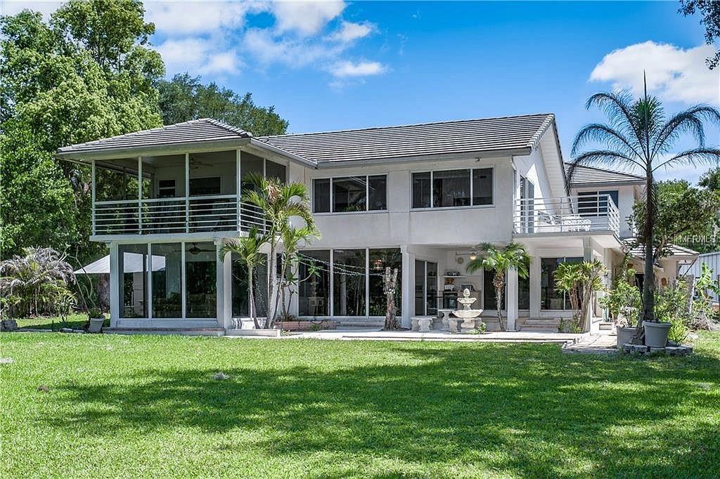 The exterior of a two-story house features a screened balcony, large windows, and palm trees — 18618 WAYNE ROAD, ODESSA, FL