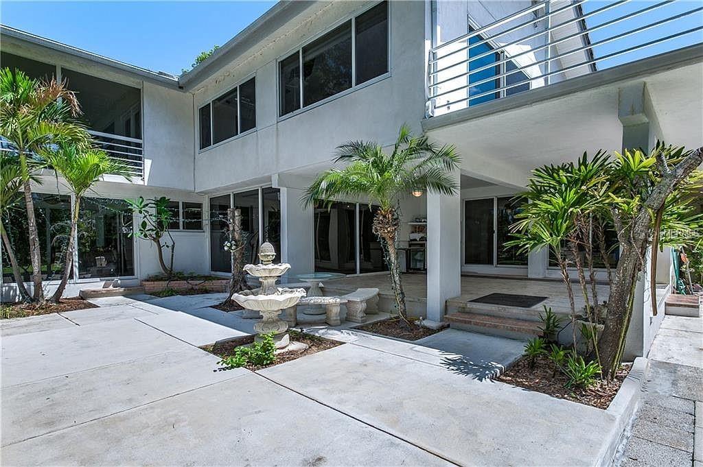 A concrete patio features a tiered fountain, palm trees, and a two-story white building — 18618 WAYNE ROAD, ODESSA, FL