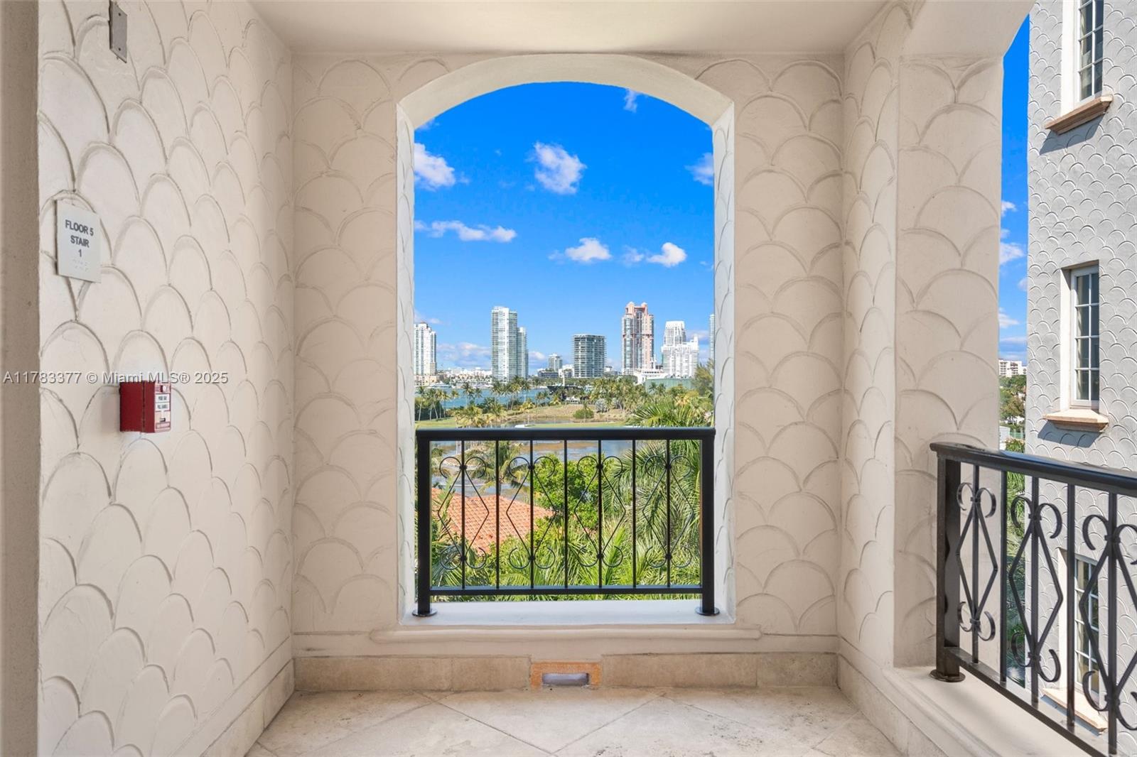 An arched balcony with textured scalloped walls overlooks a city skyline and water — FISHER ISLAND, FL