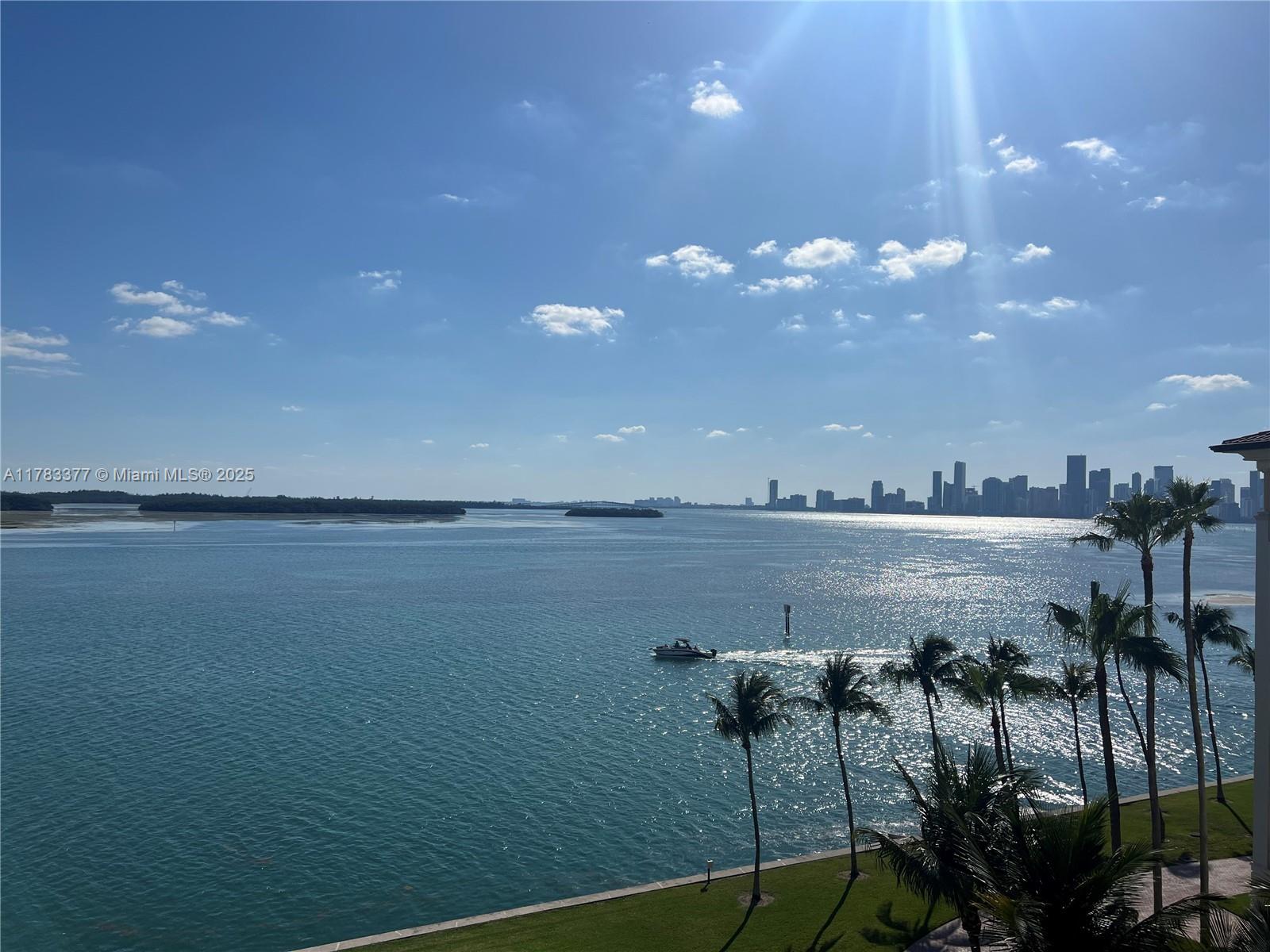 A view of a bay with a boat, palm trees, and a distant city skyline — FISHER ISLAND, FL