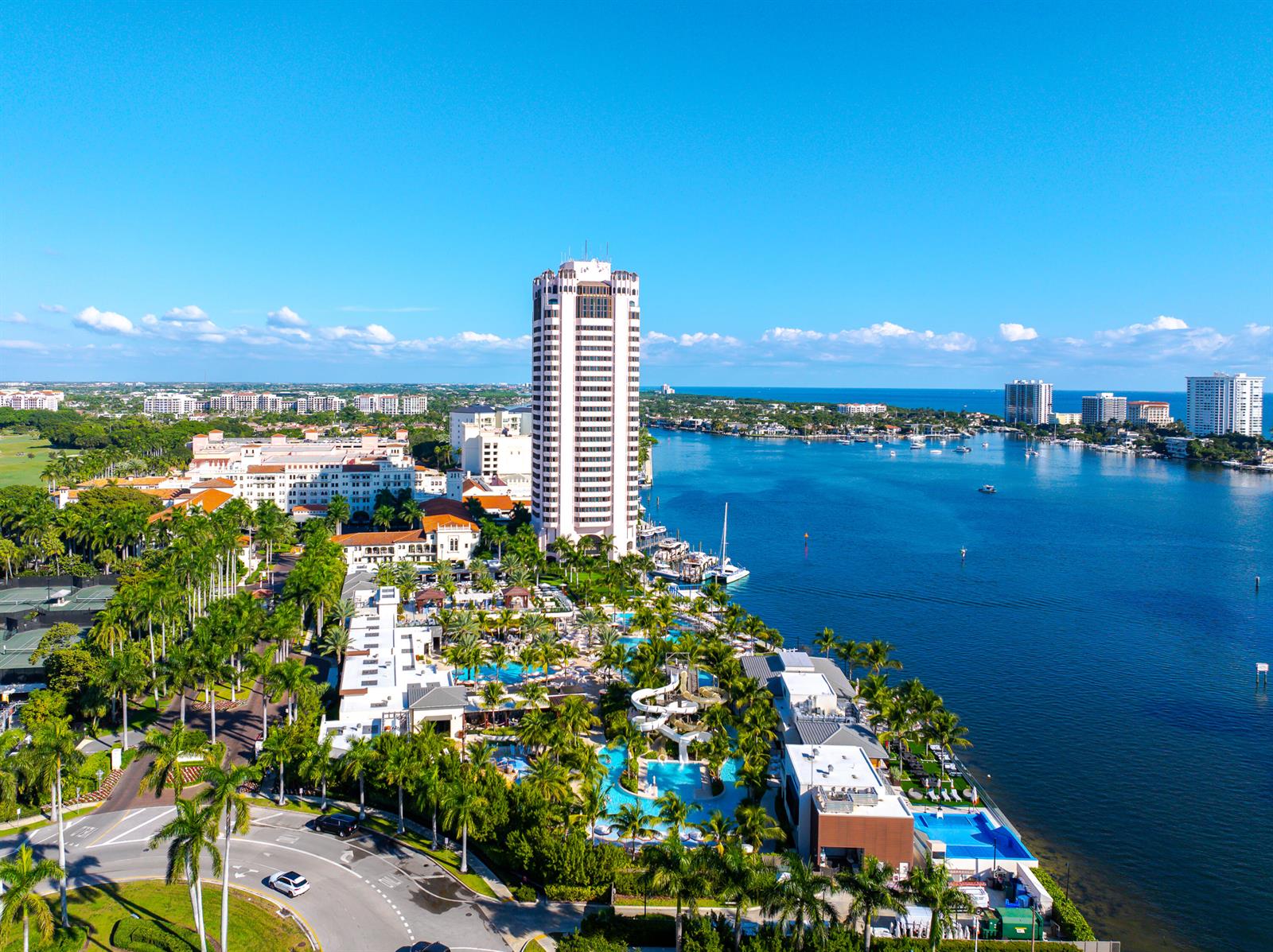An aerial view shows a tall hotel tower, swimming pools, and palm trees along a waterway — 800 E Camino Real # 309, Boca Raton FL 33432, BOCA RATON, FL