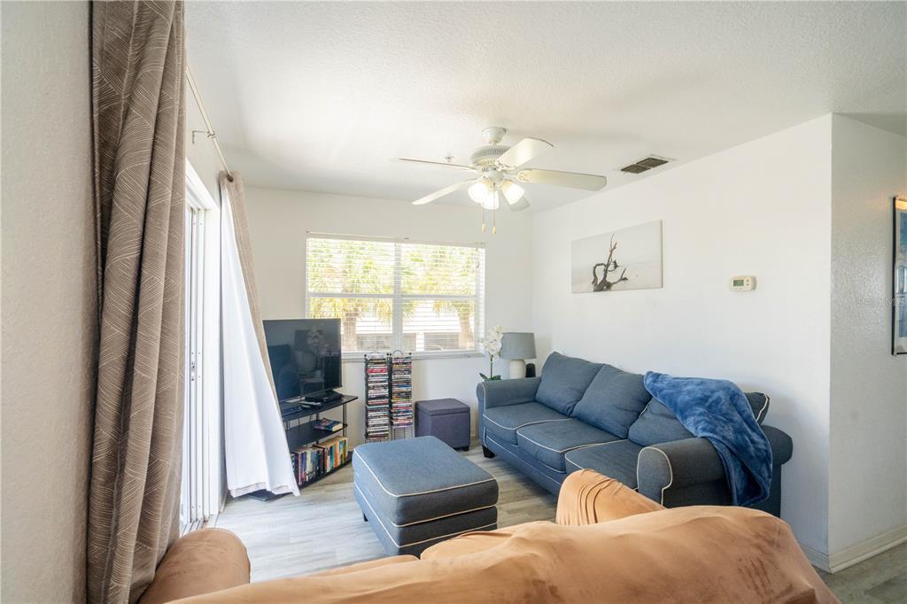 A living room features a blue sofa, matching ottoman, television, and a ceiling fan — 1802 GULF BOULEVARD UNIT 8, INDIAN ROCKS BEACH, FL