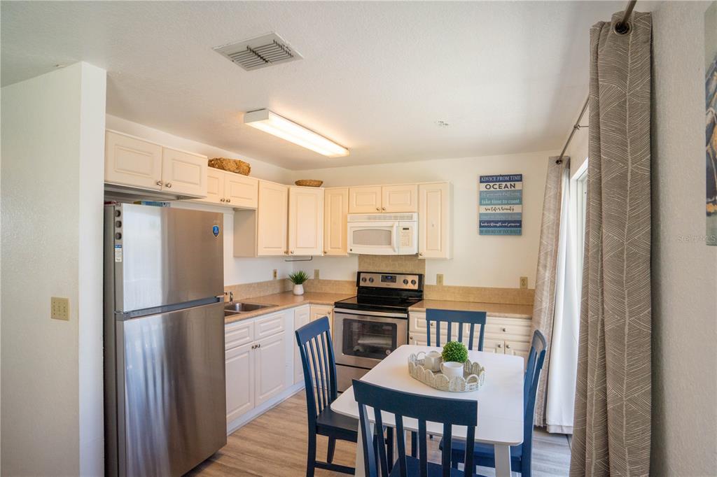 A kitchen with white cabinets, stainless steel appliances, and a small dining table with blue chairs — 1802 GULF BOULEVARD UNIT 8, INDIAN ROCKS BEACH, FL