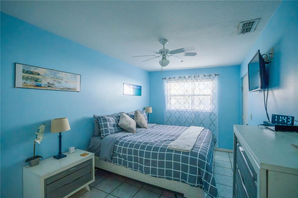 A bedroom with light blue walls, a queen bed with plaid bedding, and tile flooring — 1802 GULF BOULEVARD UNIT 8, INDIAN ROCKS BEACH, FL