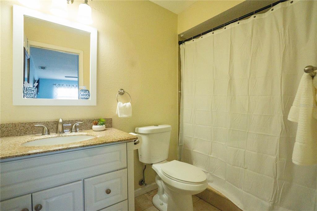 A bathroom features a white vanity with a granite countertop, a toilet, and a shower curtain — 1802 GULF BOULEVARD UNIT 8, INDIAN ROCKS BEACH, FL