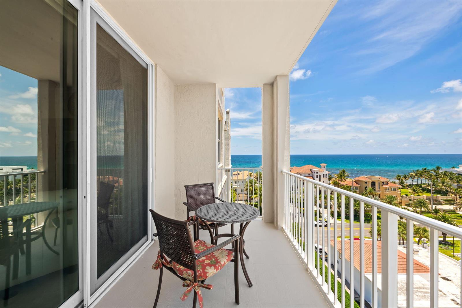 A balcony with a small table and two chairs overlooks the ocean and coastal buildings — 3606 S Ocean Boulevard # 1004, Highland Beach FL 33487, HIGHLAND BEACH, FL
