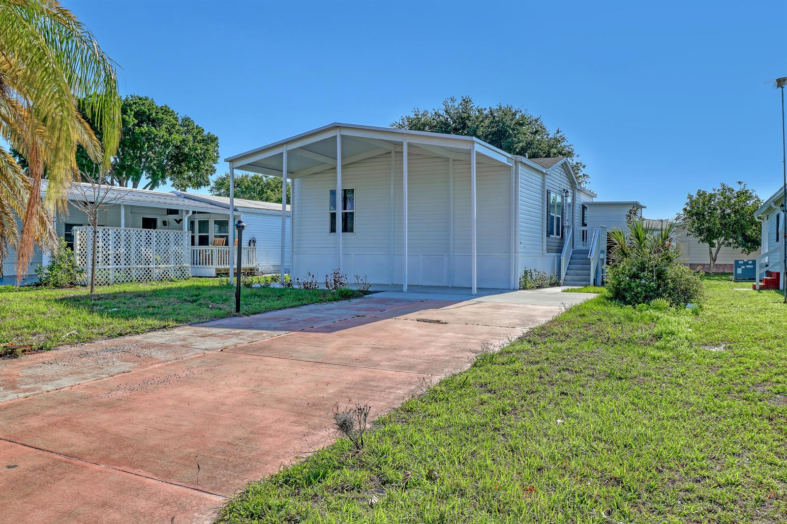 A white manufactured home features a covered carport and a concrete driveway on a sunny day — 1479 Barefoot Circle, Sebastian FL 32976, SEBASTIAN, FL