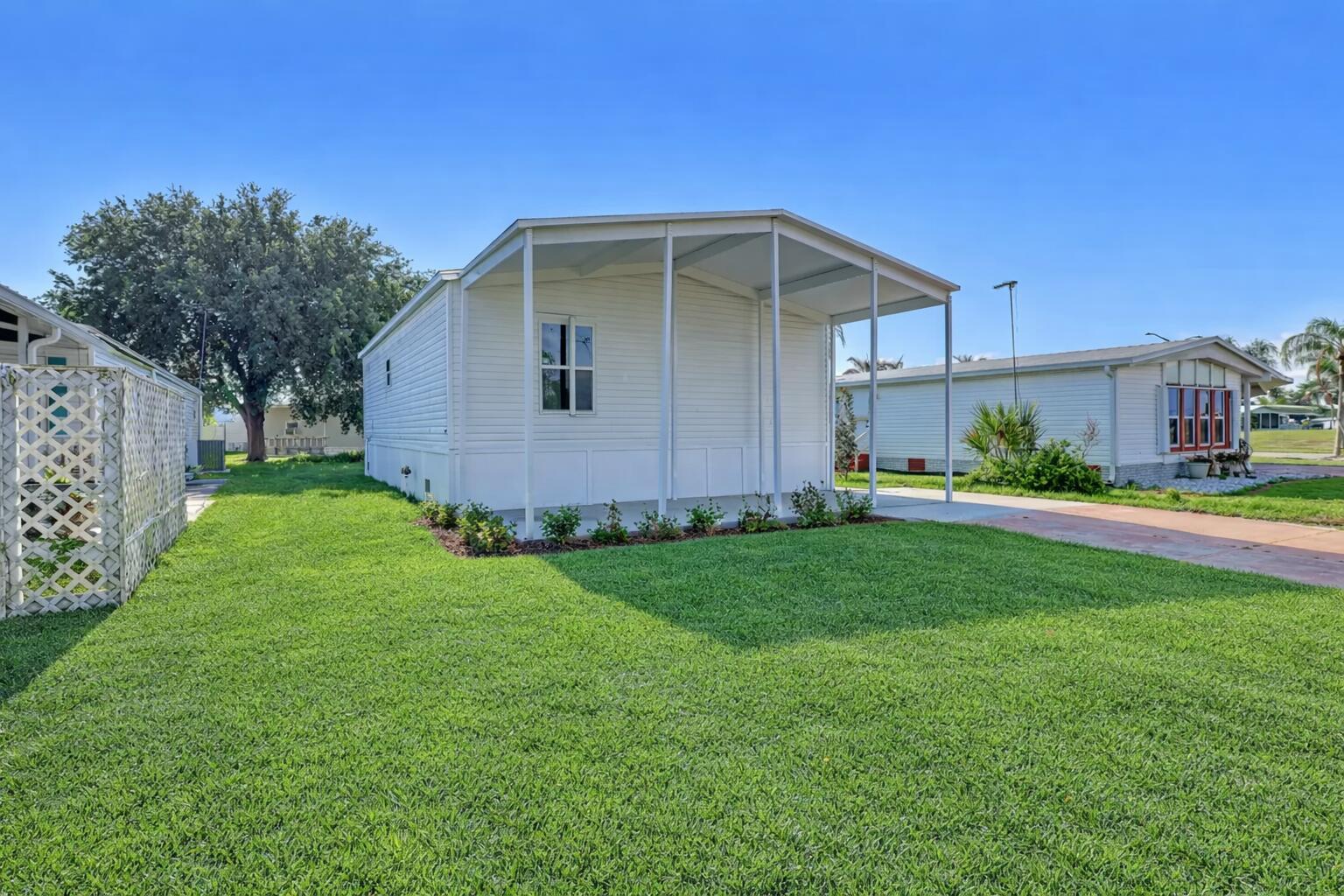 A white mobile home with a covered front porch sits on a grassy lot — 1479 Barefoot Circle, Sebastian FL 32976, SEBASTIAN, FL