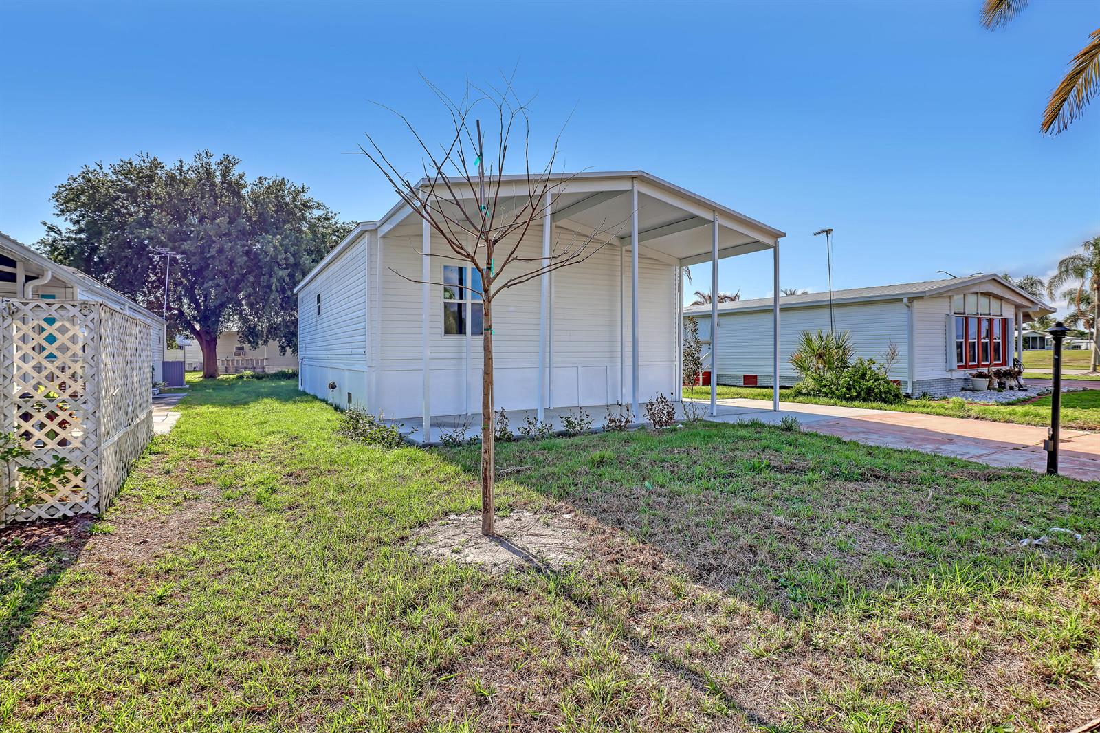 A white manufactured home with a covered carport stands on a grassy lot — 1479 Barefoot Circle, Sebastian FL 32976, SEBASTIAN, FL