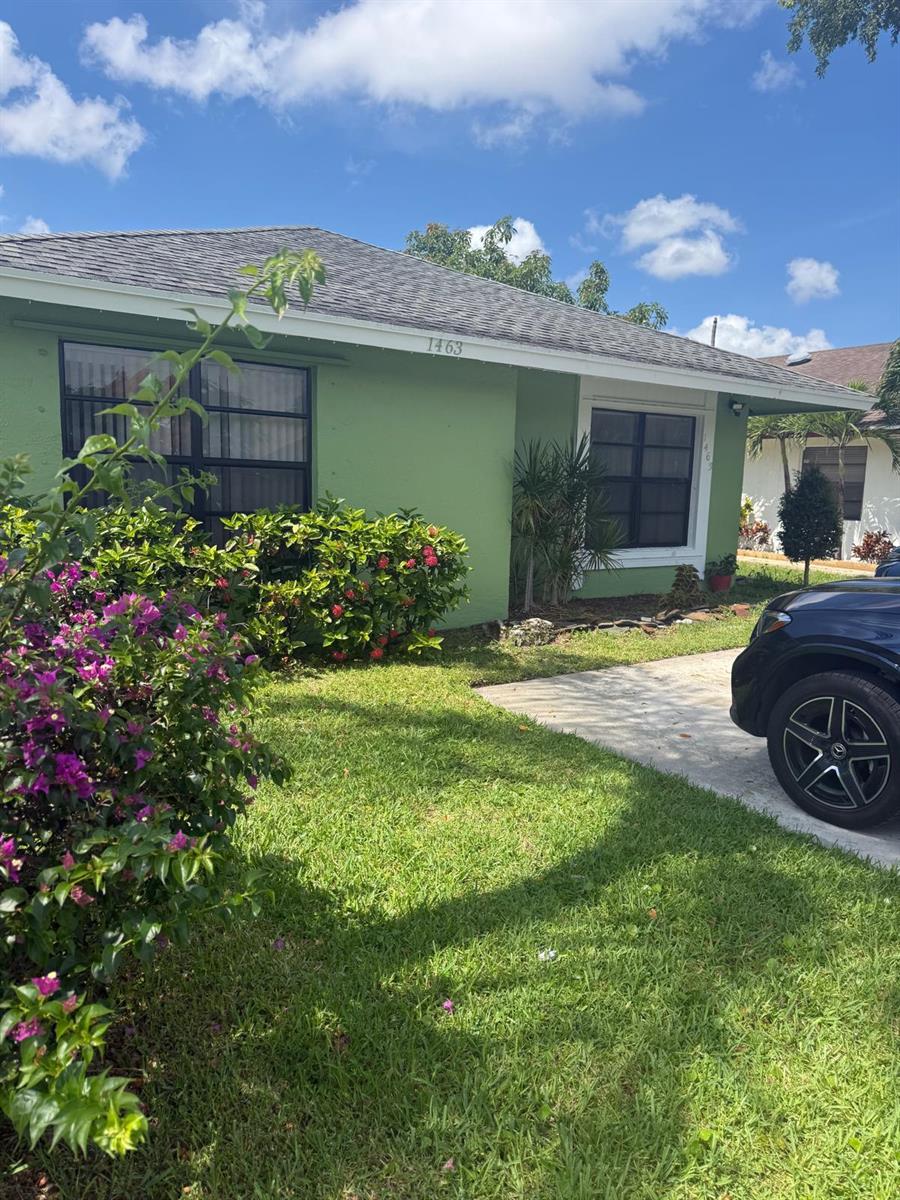 A green single-story house with a driveway and a front yard with flowering bushes — 1463 Summit Run Circle, West Palm Beach FL 33415, WEST PALM BEACH, FL