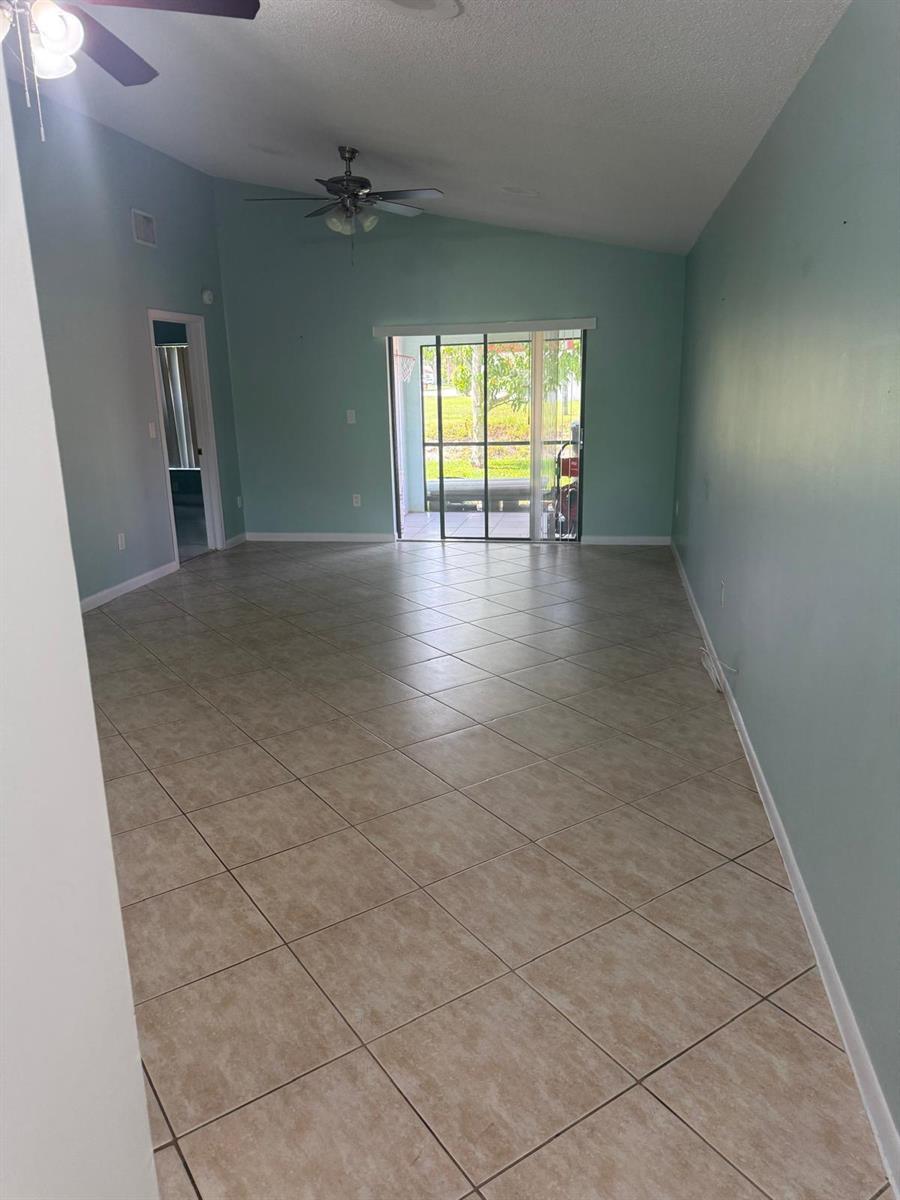 A spacious living room features light blue walls, diagonal tile flooring, and sliding glass doors — 1463 Summit Run Circle, West Palm Beach FL 33415, WEST PALM BEACH, FL