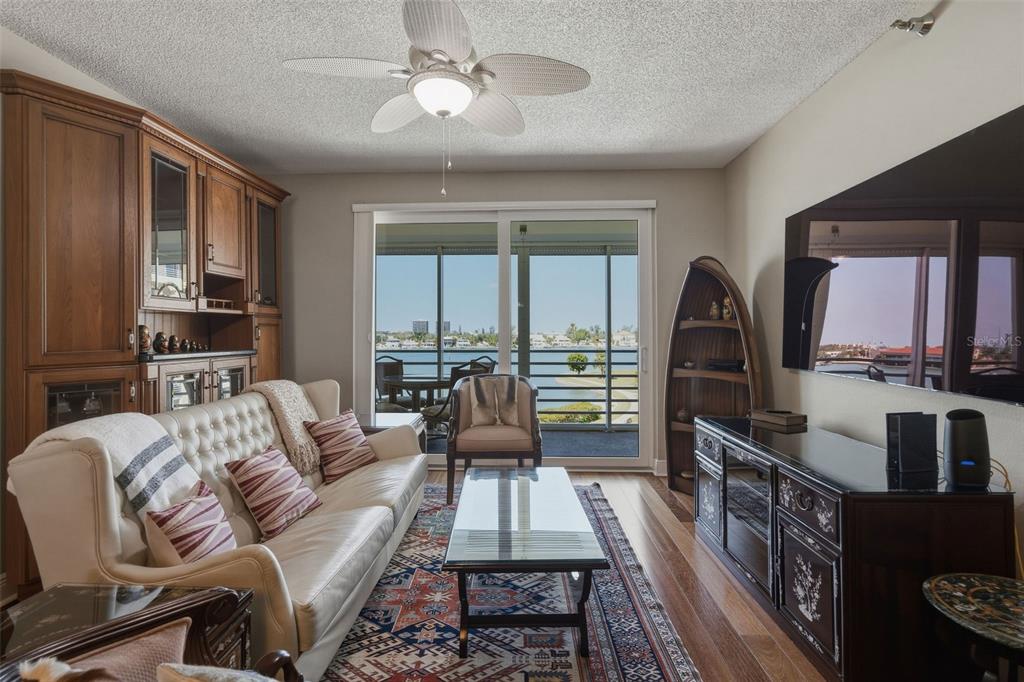 A living room features a white tufted sofa, wooden cabinetry, and a balcony overlooking water — 7872 SAILBOAT KEY BOULEVARD S UNIT 405, SOUTH PASADENA, FL