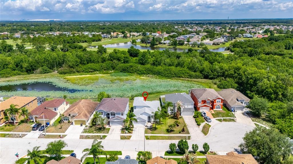 An aerial view shows a suburban neighborhood with houses bordering a pond and wooded area — 11207 VILLAGE BROOK DRIVE, RIVERVIEW, FL