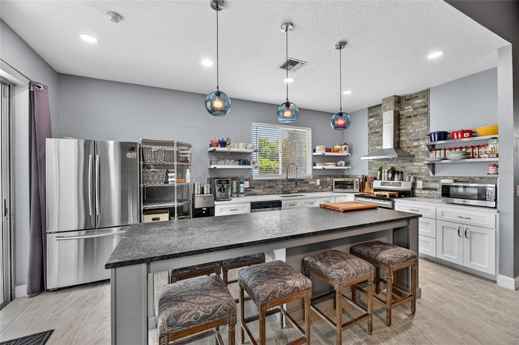 A kitchen features a large island with bar stools, stainless steel appliances, and stone backsplash — 11207 VILLAGE BROOK DRIVE, RIVERVIEW, FL