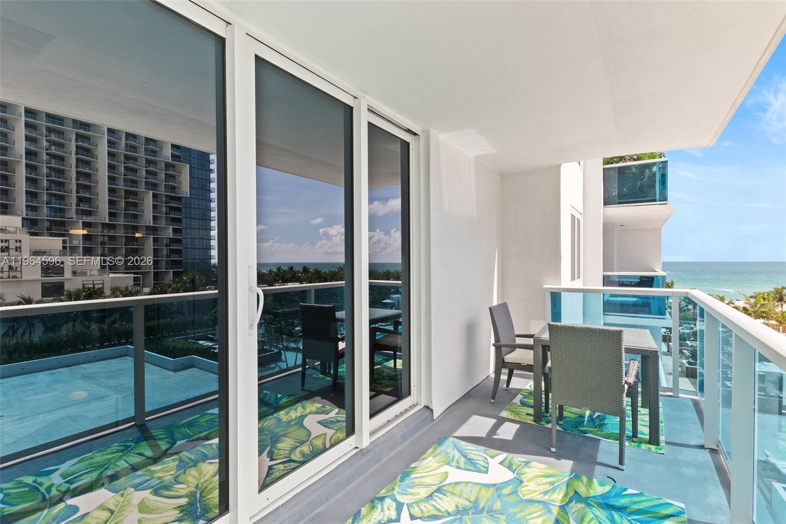 A balcony with a dining set, patterned rugs, and glass railings overlooking the ocean — 2301 Collins Ave # 504, Miami Beach FL 33139, MIAMI BEACH, FL
