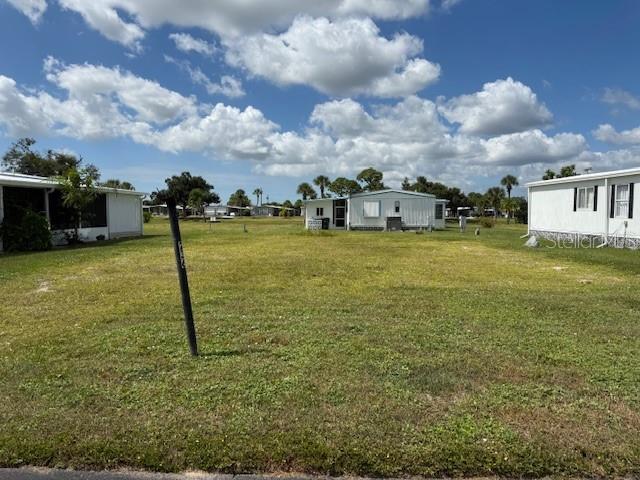 A vacant grassy lot sits between two manufactured homes under a blue sky with clouds — 236 LA ROSAS, NORTH PORT, FL