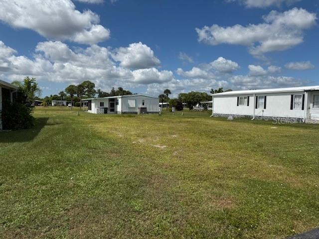 A vacant grassy lot sits between two manufactured homes under a blue sky with clouds — 236 LA ROSAS, NORTH PORT, FL