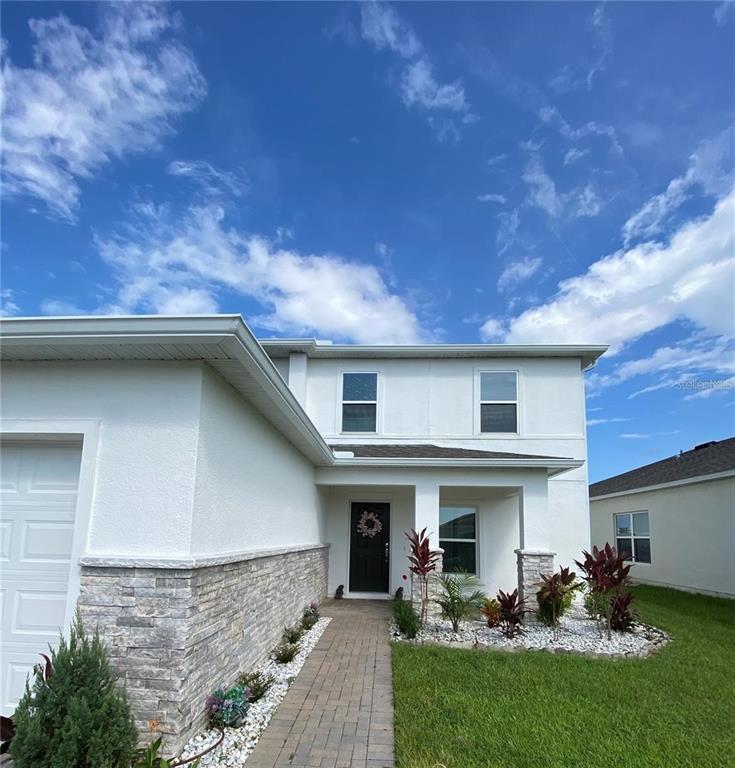 A two-story house exterior features white stucco walls, stone veneer accents, and a paved walkway — 247 SPARROW HAWK DRIVE, GROVELAND, FL