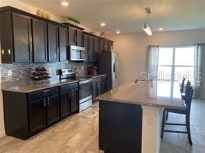 A kitchen features dark wood cabinets, granite countertops, a center island, and stainless steel appliances — 247 SPARROW HAWK DRIVE, GROVELAND, FL
