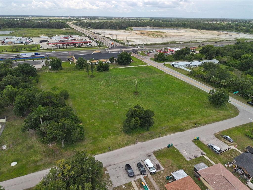 An aerial view shows a large, grassy vacant lot bordered by roads and nearby commercial buildings — 3700 BAYSWATER DRIVE, PUNTA GORDA, FL