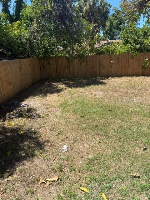 A backyard features a wooden fence, patches of grass, and scattered leaves under trees — 408 N MARTIN LUTHER KING JR AVENUE, CLEARWATER, FL