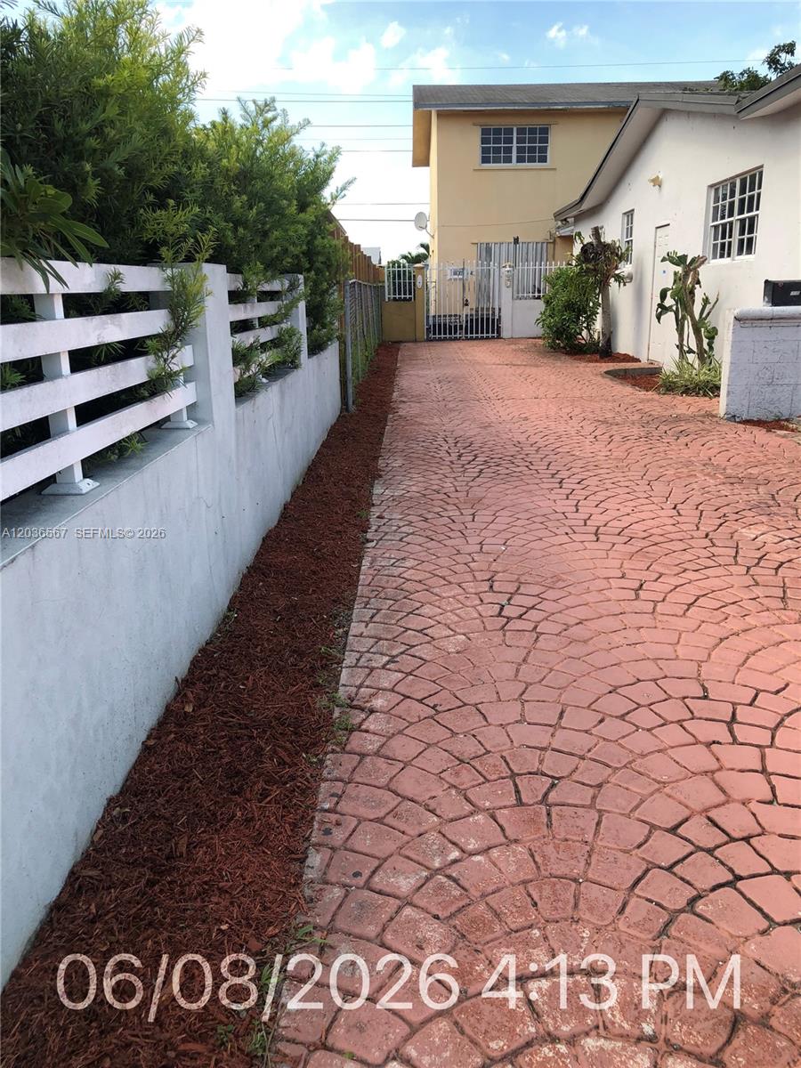 A paved driveway runs alongside a white wall and a house with a gate — 447 E 32nd St, Hialeah FL 33013, HIALEAH, FL