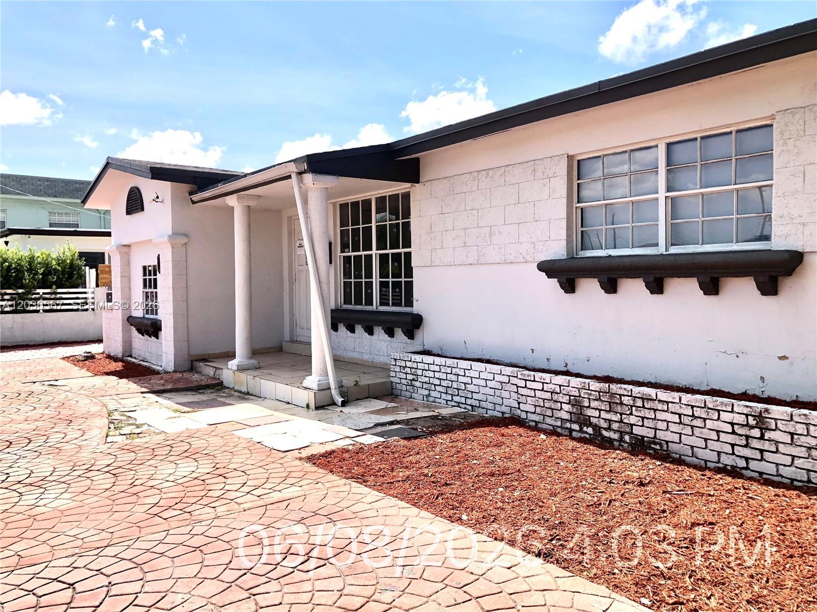 The exterior of a white house features a paved driveway, a covered porch, and brick accents — 447 E 32nd St, Hialeah FL 33013, HIALEAH, FL