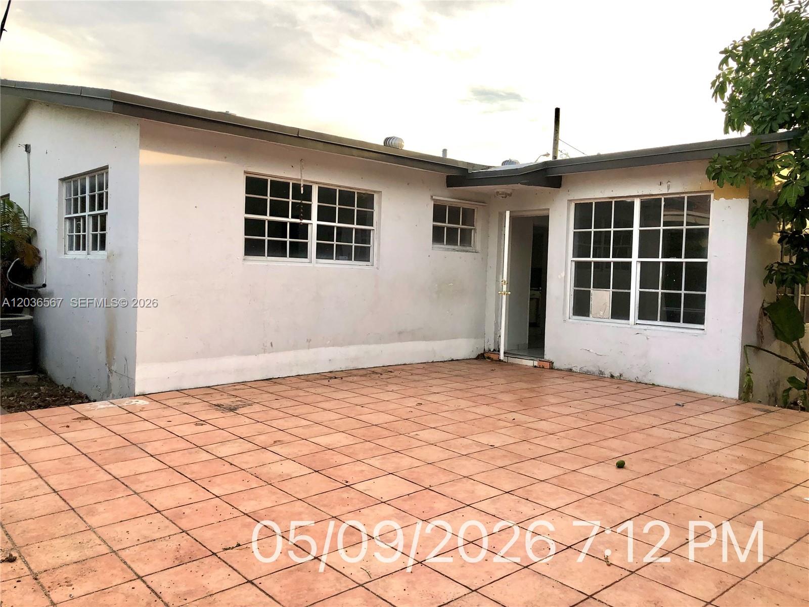 The exterior of a white house features a tiled patio and several grid-patterned windows — 447 E 32nd St, Hialeah FL 33013, HIALEAH, FL