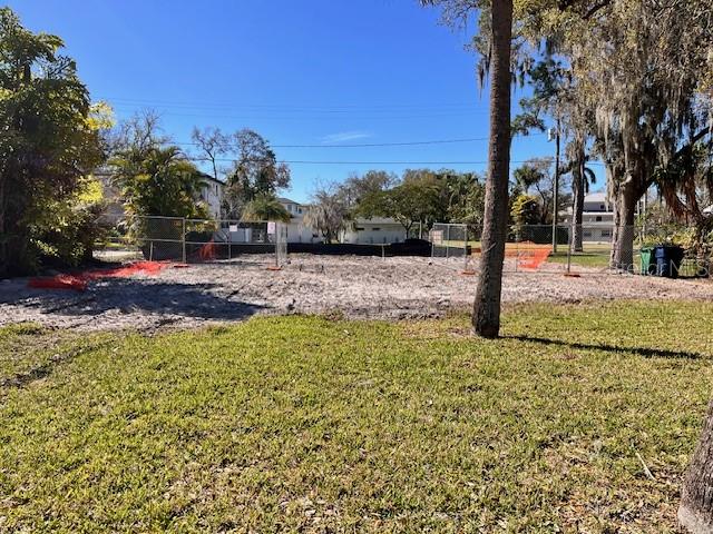 A vacant, fenced-in lot with sandy ground is surrounded by trees and residential buildings — 2640 S DUNDEE STREET, TAMPA, FL
