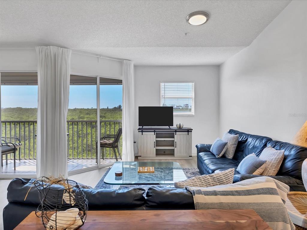 A living room features a dark leather sofa, glass coffee table, and a balcony view — 3607 E BAY DRIVE UNIT 206, BRADENTON BEACH, FL
