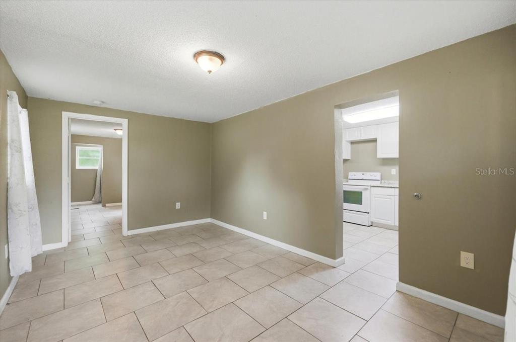 A room with beige walls and light-colored tile flooring leads into a kitchen — 2418 JUNGLE STREET, LAKELAND, FL
