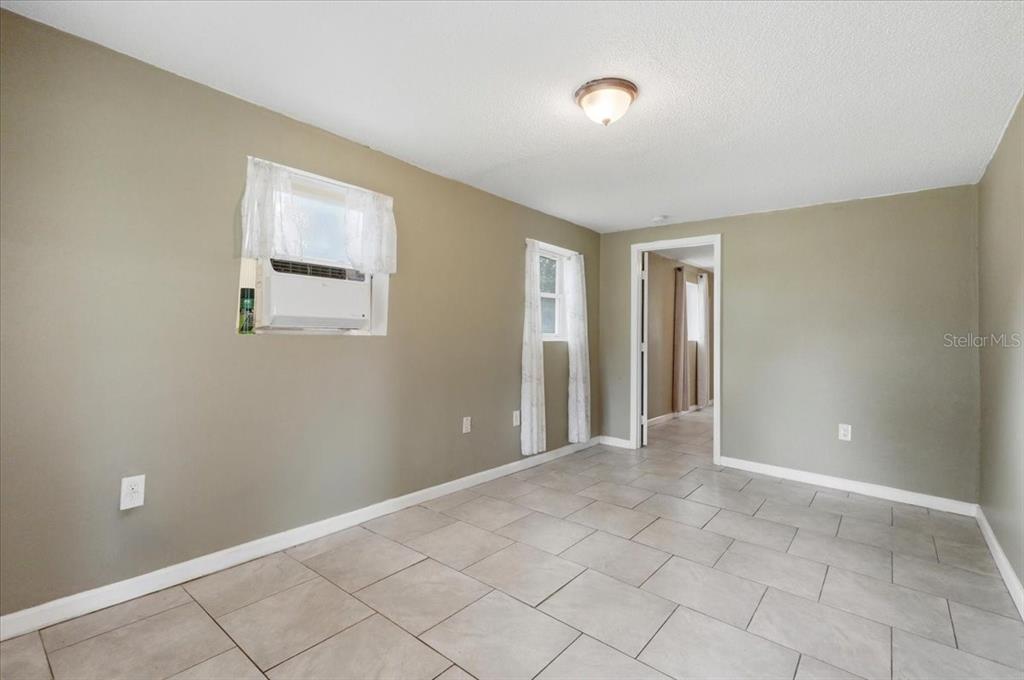 A room with light-colored tile flooring, tan walls, two windows, and a doorway — 2418 JUNGLE STREET, LAKELAND, FL
