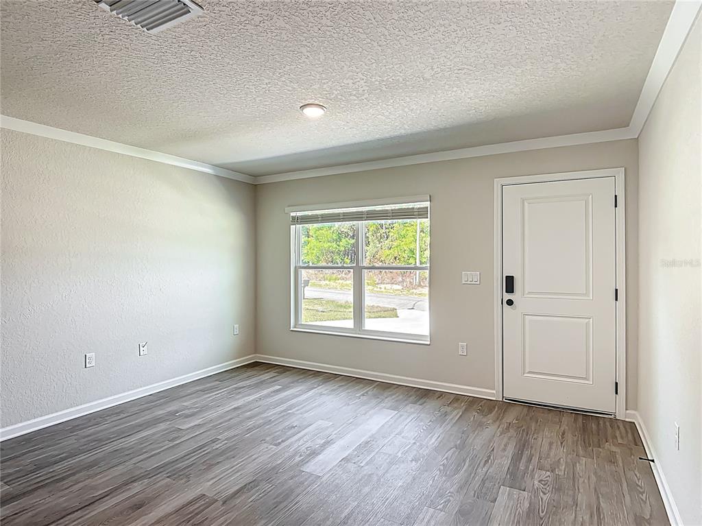 An empty room features light-colored walls, wood-look flooring, a window, and a white entry door — 15845 SW 33RD AVENUE ROAD, OCALA, FL