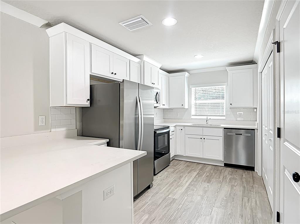 A kitchen with white cabinets, stainless steel appliances, and light wood-look flooring — 15845 SW 33RD AVENUE ROAD, OCALA, FL