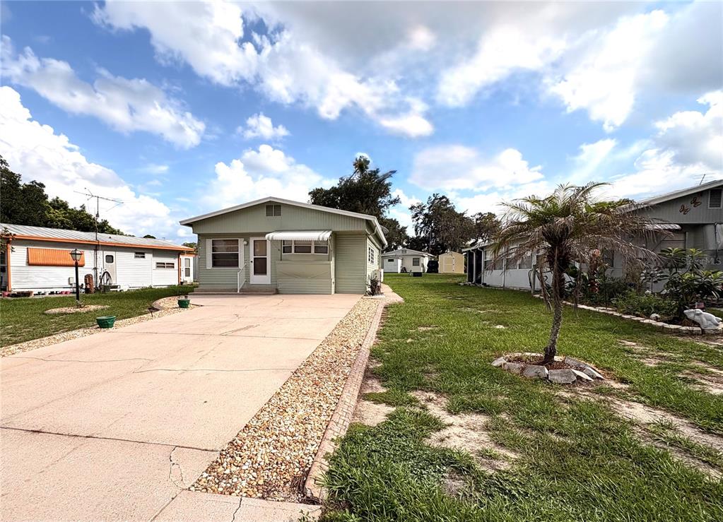 A light green manufactured home with a concrete driveway and a small palm tree — 117 SADDLEBAG TRAIL, LAKE WALES, FL