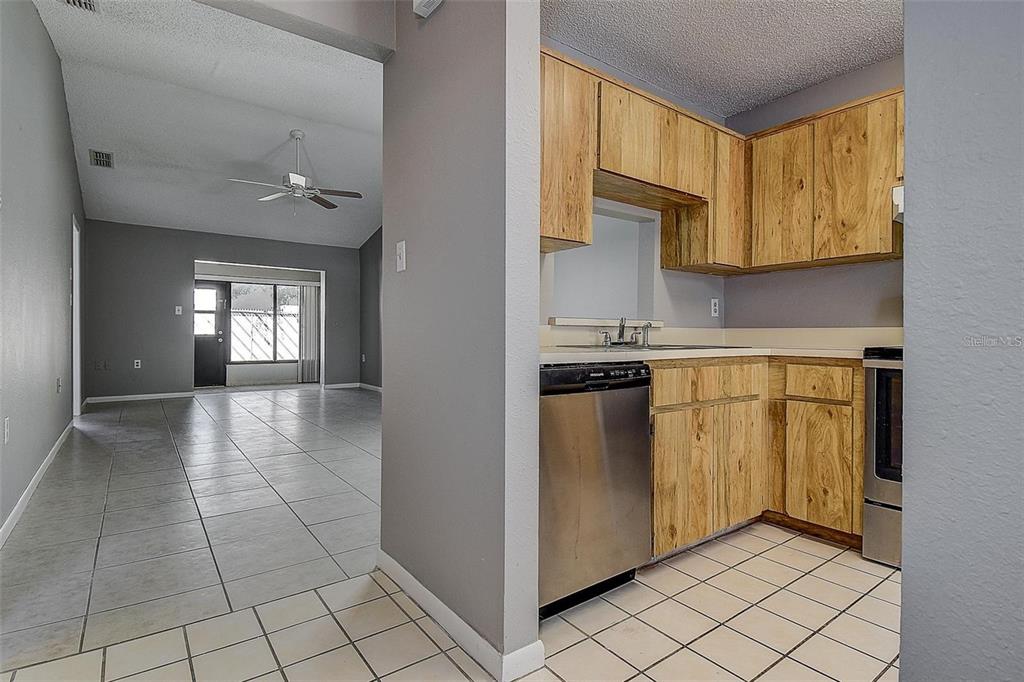 A kitchen with wood cabinets and stainless steel appliances opens into a tiled living area — 4752 SUNNY LOOP, HOLIDAY, FL