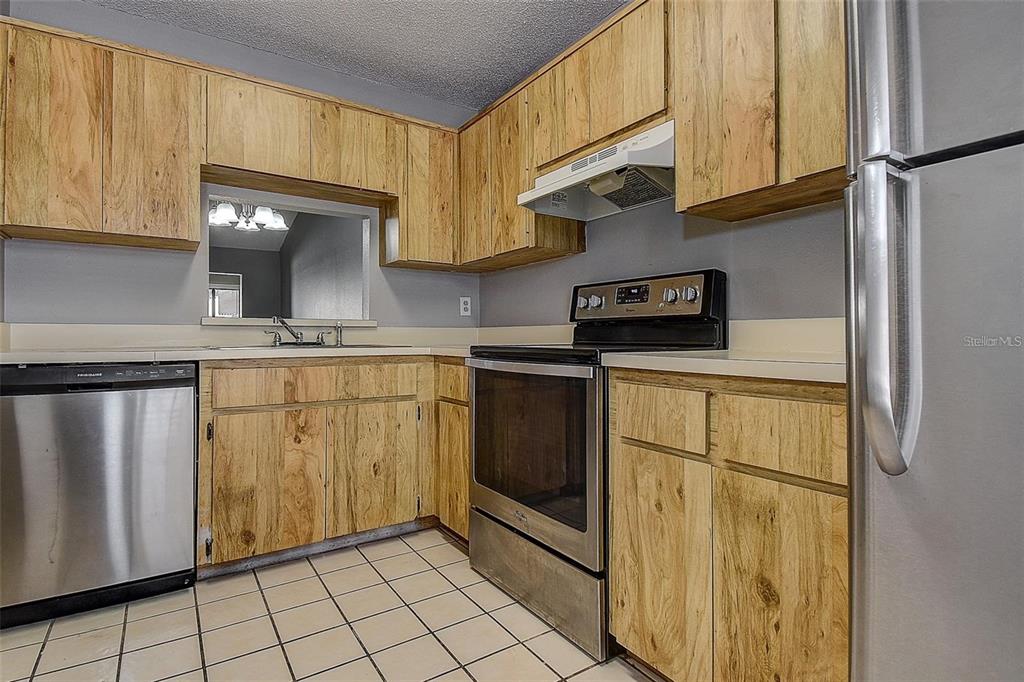 A kitchen features wood-grain cabinets, stainless steel appliances, and light-colored tile flooring — 4752 SUNNY LOOP, HOLIDAY, FL