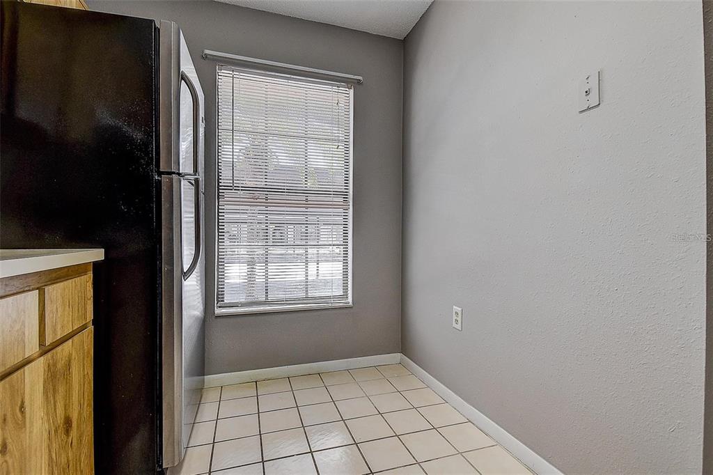 A kitchen nook features a black refrigerator, a window with blinds, and tiled flooring — 4752 SUNNY LOOP, HOLIDAY, FL