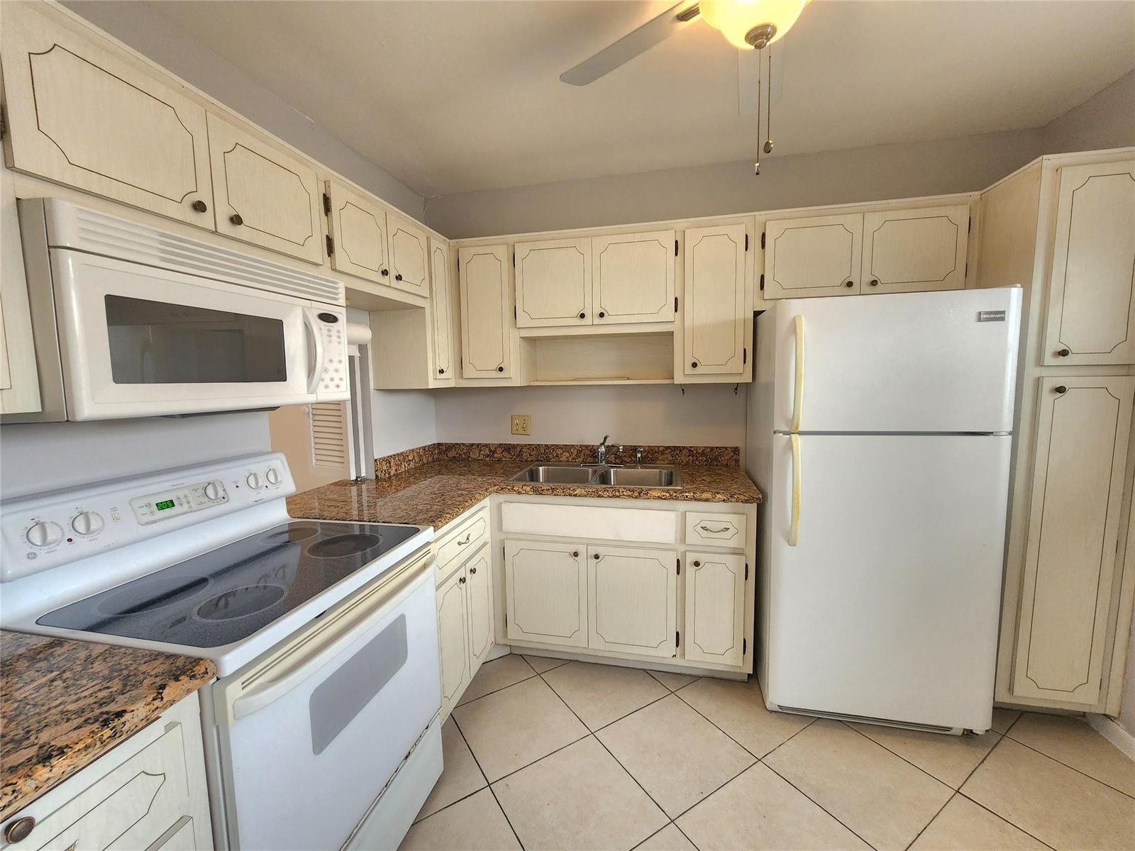 A kitchen features off-white cabinets, granite countertops, white appliances, and light-colored tile flooring — 2223 Park Lane # 105, Hollywood FL 33021, HOLLYWOOD, FL