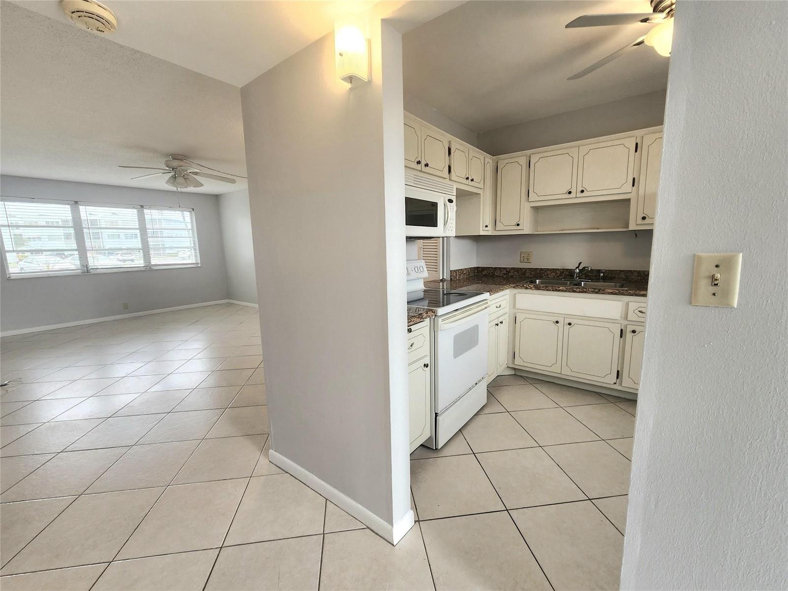 A kitchen with white cabinets and tile floors opens into a spacious living area — 2223 Park Lane # 105, Hollywood FL 33021, HOLLYWOOD, FL