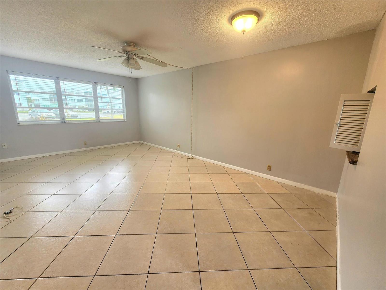 An empty room features beige tile flooring, a ceiling fan, and a large window — 2223 Park Lane # 105, Hollywood FL 33021, HOLLYWOOD, FL