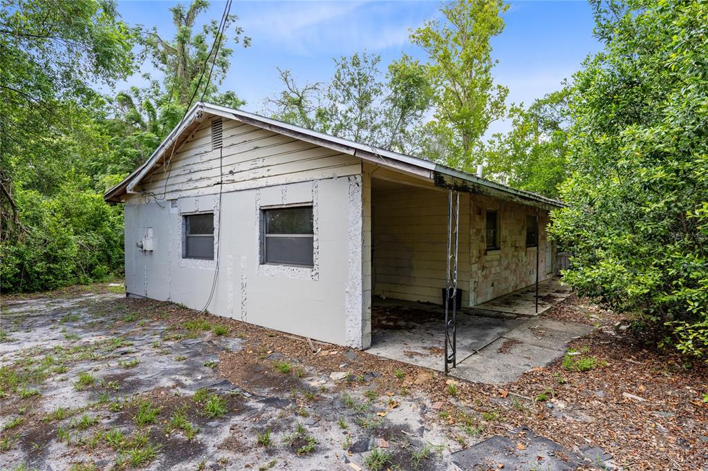 A weathered, single-story house with a carport and stone siding sits on a wooded lot — 3711 N RONALD REAGAN BOULEVARD, LONGWOOD, FL