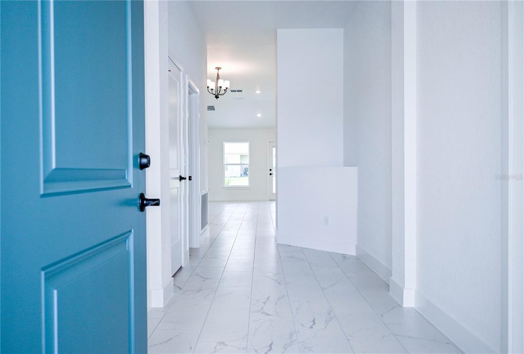 A bright entryway with a blue door leads into a hallway featuring white tiled floors — 3139 NE 45TH AVENUE, OCALA, FL