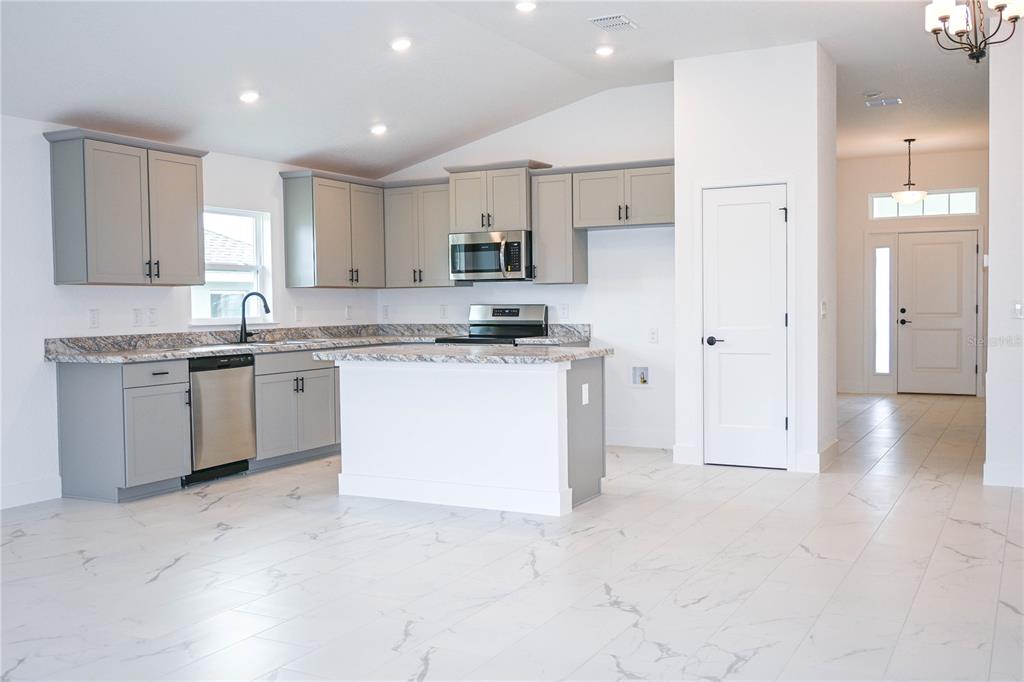 A kitchen with grey cabinets, granite countertops, and a white island on marble-look tile flooring — 3139 NE 45TH AVENUE, OCALA, FL