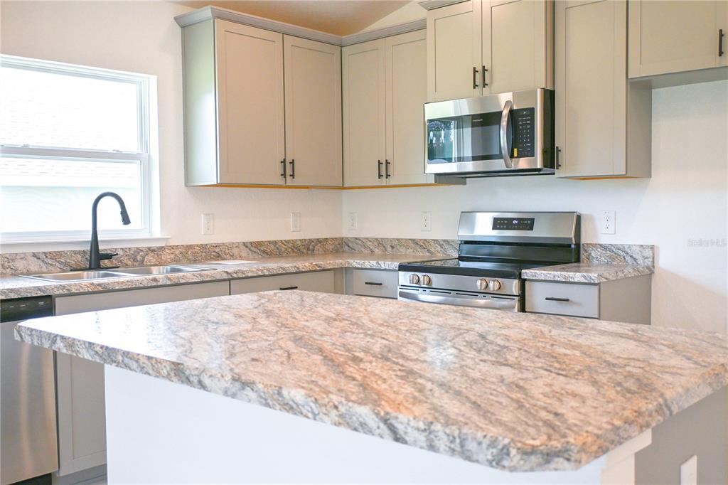 A kitchen features light gray cabinets, granite countertops, and stainless steel appliances — 3139 NE 45TH AVENUE, OCALA, FL